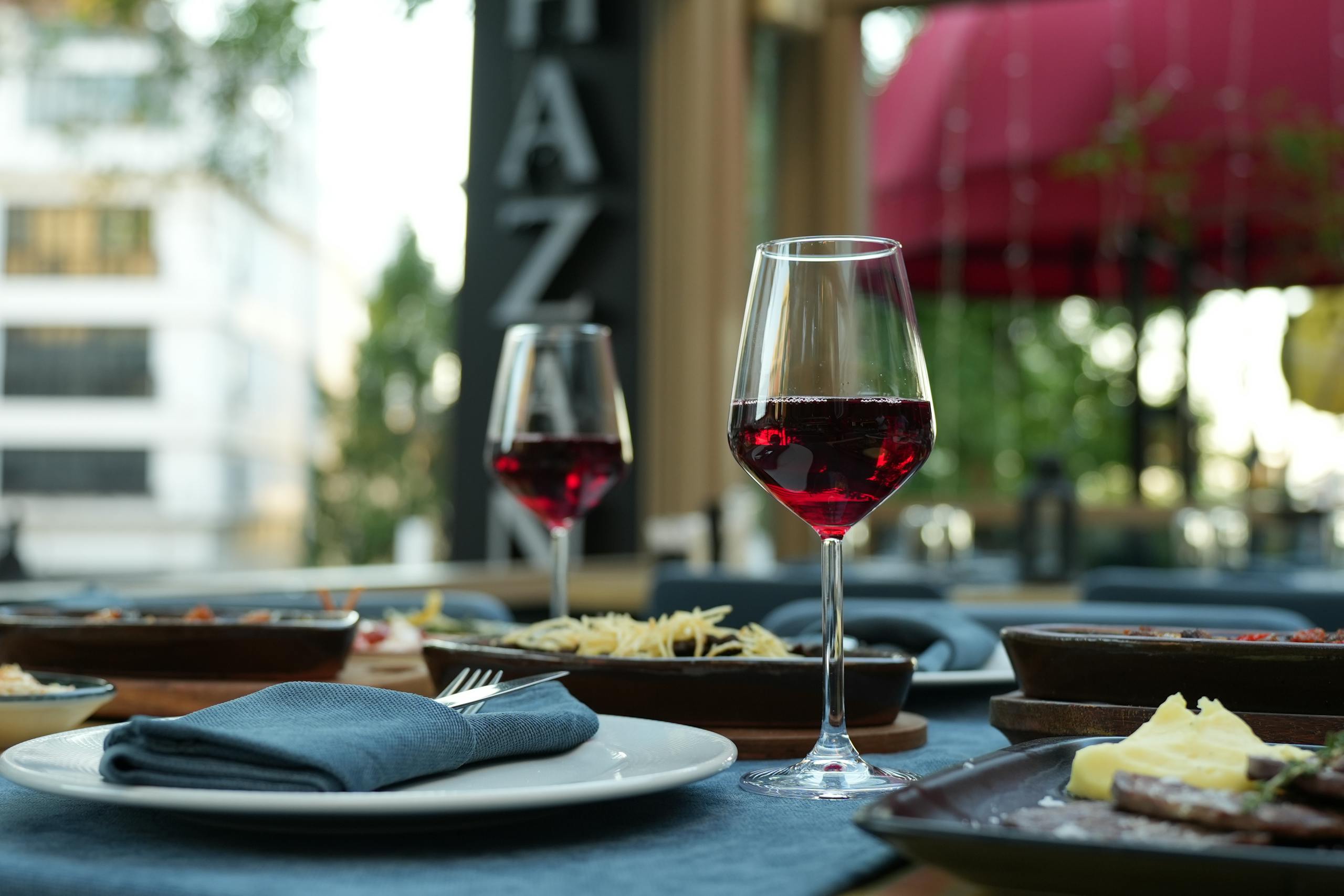 A sophisticated dining setup featuring red wine, gourmet dishes, and a casual outdoor atmosphere.